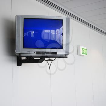 Monitor mounted to wall next to exit sign in airport
