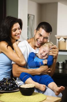 Royalty Free Photo of a Caucasian Family With Toddler Son in the Kitchen at Breakfast Smiling and Tickling