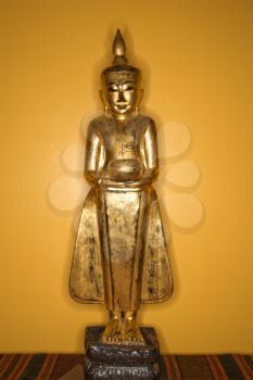 Royalty Free Photo of a Golden Wooden Buddha Statue From Myanmar Against a Yellow Wall