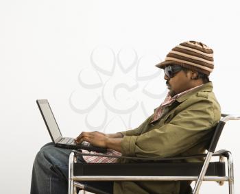 Royalty Free Photo of a Man Wearing a Hat and Typing on a Laptop Computer
