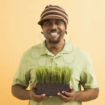 Royalty Free Photo of an African American Man Wearing Hat Holding Potted Grass Smiling