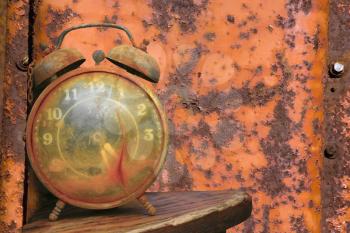 Old weathered alarm clock against rusty orange metal background.