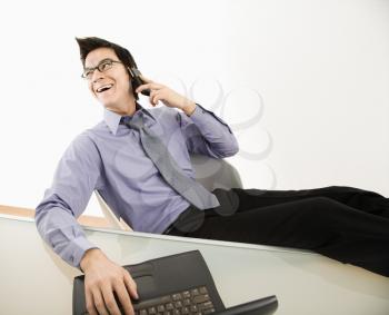 Royalty Free Photo of a Laughing Businessman Sitting at a Desk Talking on a Cellphone