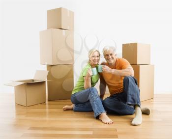 Royalty Free Photo of a Middle-aged Couple Sitting on a Floor Among Cardboard Moving Boxes Drinking Coffee