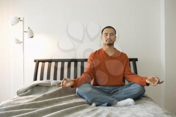 Young Asian man sitting on bed in the lotus position. Horizontal shot.