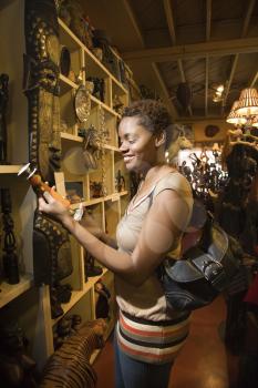 Smiling African American woman standing and looking at a candlestick or vase in a retail display. Vertical format.