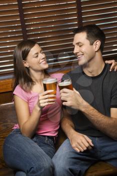 Young man and woman sitting together toasting their beers while relaxing at a pub. Vertical shot.