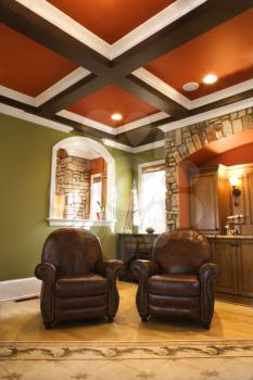 Two brown leather chairs in an upscale living room with wooden box beam ceiling and stone arch accents. Vertical shot.