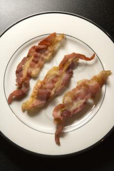 Three strips of cooked bacon in a row on a white plate. Vertical shot.