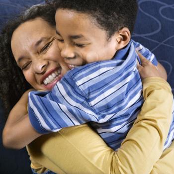 A mid adult African American woman affectionately hugs her young son. Square shot.