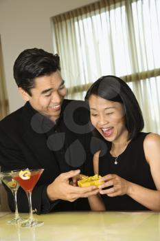 Young Asian man presents a small gift to an attractive Asian woman at a bar. Vertical shot.
