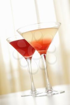 Two red colored mixed drinks in martini glasses on a table. Vertical shot.