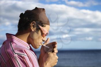 Close-up of a young man standing by the ocean and lighting a cigarette. Horizontal shot.