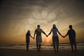 Silhouette of family holding hands on beach watching the sunset. Horizontally framed shot.