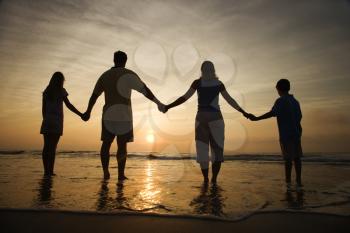 Silhouette of family holding hands on beach watching the sunset. Horizontally framed shot.