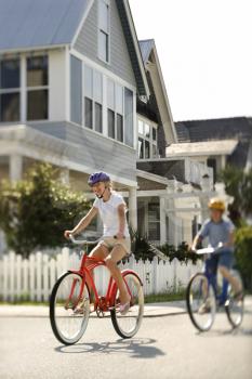 Two teens ride bicycles through a residential neighborhood. Vertical shot.