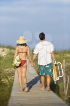 Rear view of a man and woman holding hands, walking down a beach boardwalk. Vertical shot.