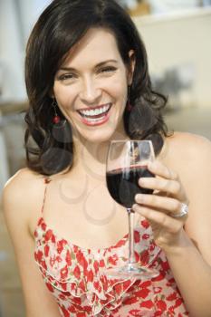 Woman toasts the camera with a glass of red wine. Vertical shot.