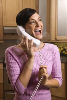 Woman smiling and talking on the telephone in the kitchen.  Vertical shot.