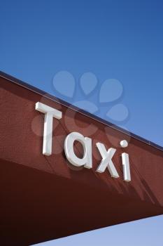 Taxi sign on a brown roof wall facade with a clear blue sky in the background. Vertical shot.