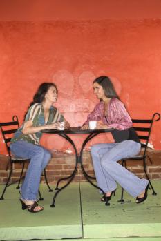 Two young adult women sitting in a cafe, having coffee and talking. Vertical shot.