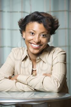 Portrait of an attractive African-American young woman. She has her arms crossed on the table and is smiling at the camera. Vertical shot.