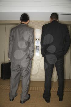 Rear view of two young adult businessmen waiting for an elevator. Vertical format.