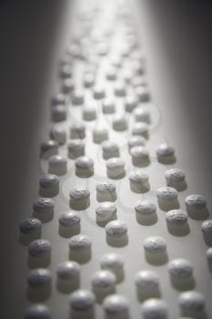 White round pills illuminated by a shaft of light. Vertical shot.