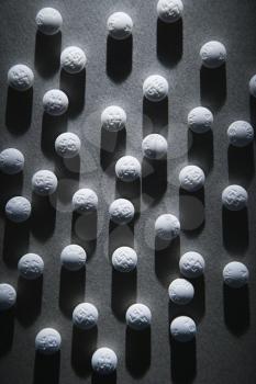 Close up of round white pills in a shaft of light, casting a shadow. Vertical shot.
