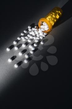 Yellow medicine bottle with round white pills spilling out. A shaft of light illuminates the pills. Vertical shot.