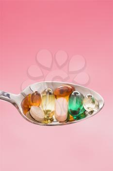 Silver spoon with different types of pills. Vertical shot. Isolated on pink.