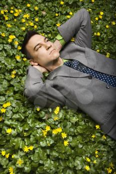 Young businessman with relaxing in a flower patch thinking. Vertical shot.