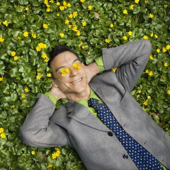 Young smiling businessman relaxing in a flower patch with flowers over his eyes.
