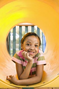 Young girl lying in yellow crawl tube at playground and smiling.