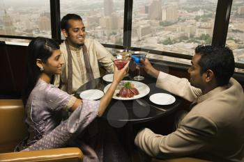 High angle view of young adult males and a female seated near a window of a high rise restaurant. They are toasting with martinis. Horizontal shot.