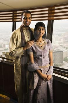 Portrait of a young adult couple standing near a high rise window and smiling at the camera. Vertical shot.