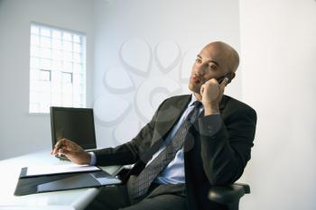 African American businessman sitting at office desk talking on cellphone.