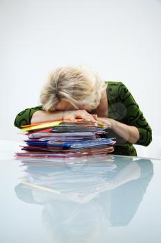 Caucasian middle aged businesswoman sitting at office desk with head down on top of pile of folders.