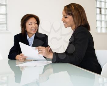 Two businesswomen sitting at office desk having meeting and discussing paperwork.