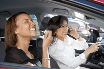 Women distracted and laughing in car with cellphone and cosmetics.