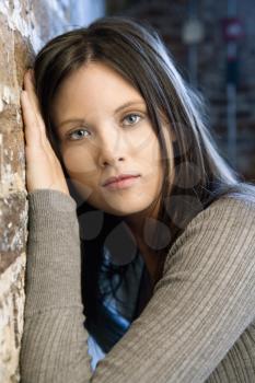 Portrait of pretty young Caucasian woman leaning against brick wall.