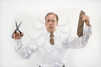 Caucasian middle aged businessman holding cut off necktie and scissors.