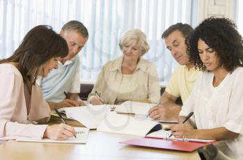 Royalty Free Photo of Five Adults Writing in Books at a Table