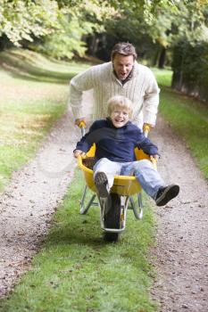 Royalty Free Photo of a Father Pushing a Boy in a Wheelbarrow