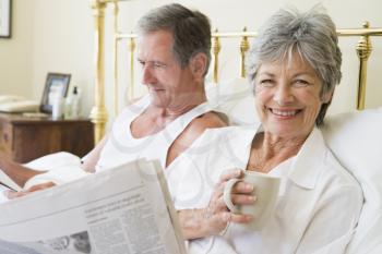 Royalty Free Photo of a Couple Reading the Newspaper in Bed