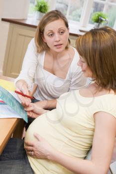 Royalty Free Photo of a Pregnant Woman Reading a Pamphlet With Another Woman