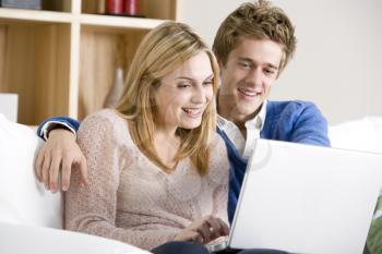 Young Couple Sitting On Sofa Using Laptop