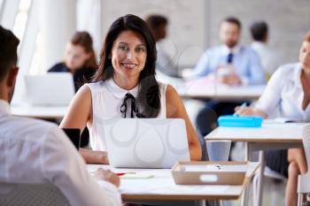 Portrait Of Businesswoman Working On Laptop In Busy Office