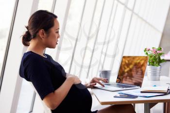 Pregnant Businesswoman Using Laptop In Office