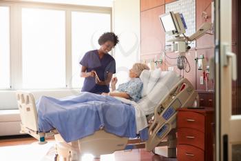 Hospital Nurse With Digital Tablet Talks To Senior Patient